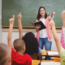 photo of teacher in front of class with students with raised hands